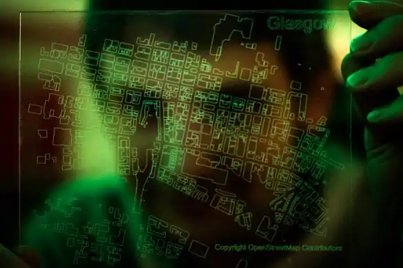 a transparent laser-etched acrylic map of OpenStreetMap buildings in central Glasgow with a green glow and a person behind