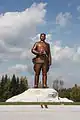 1/4 Statue of Kim Il-sung (artwork_type=statue and tourism=artwork) on its white base with trees in the background seen from the ground.