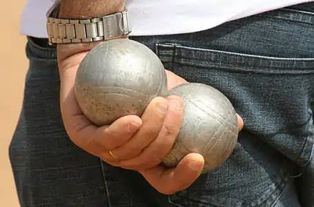 Un joueur de Pétanque tiens deux boules dans son dos.