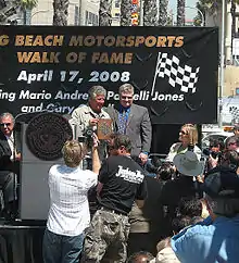 A ceremony where a retired racing driver receives a plaque from a city official