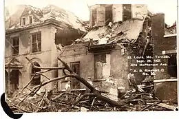 Black-and-white photograph with beige tint showing downed tree limbs and wrecked roofs