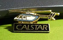 Photo of a c. 1986 CALSTAR lapel pin in black and gold featuring an MBB 135 medical helicopter in the CALSTAR colors white and blue