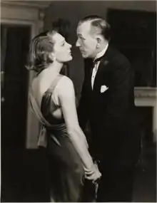 Youngish white couple in evening dress standing close together and looking into each others' eyes; greyscale.