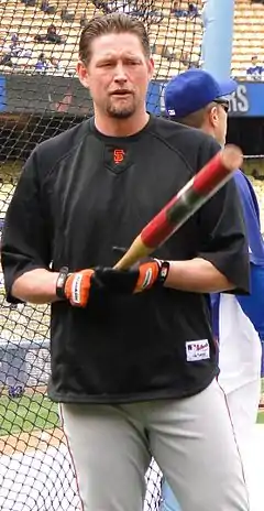 A man in a black baseball uniform pointing a bat towards the camers
