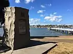 Stone monument on a bayside, with a jetty in the background