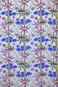 Fabric decorated with a busy design of diamonds constructed from light green bamboo stems and blue, pink and purple flowers on a white background.