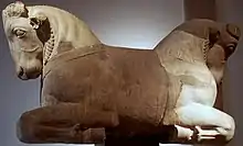 Two images representing architectural elements, the top image shows a column capital with bull protomes jutting out from its two sides. The bottom image shows torus shaped column elements laying in a green field.