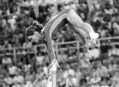 woman above a bar holding onto it during a gymnastics routine