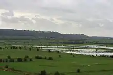 Water on grassy lowland with hills in the distance.