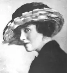 A white woman with dark hair, wearing a large brimmed hat and a dark jacket