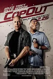Two smiling middle-aged cops stand in front of a background covered in bullet holes.