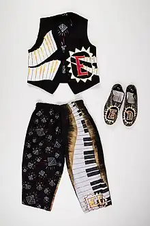 Layed flat on a white background is a waistcoat, trousers and shoes. All with decoarive elements - styalized keyboards, patterns and a funky hand-drawn E with a triangle border on the waistcoat.