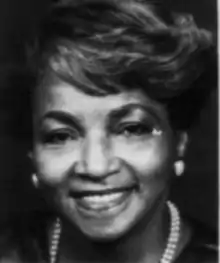 A smiling Black woman with sideswept bangs, wearing pearls and pearl earrings