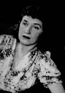 A white woman with a curled hairstyle, wearing a print dress with short sleeves