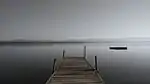A dock extends from the shore of an extremely wide river.