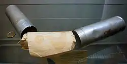 Two metal canisters resting on a glass shelf with a roll of papers, on which a question mark is visible, in between them. A two-euro coin is positioned to the left to provide a scale.