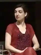 Batuman, seated, shown from the waist up wearing red, looks to her right