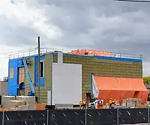 Photo of a light rail and subway station entrance under construction. White cladding panels have been affixed to a small portion of the the exterior.