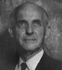 A middle-aged white man, bald, wearing a suit and necktie