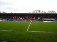 Bury F.C.'s blue stadium seated stand covered in red, white and black F.C. United banners.
