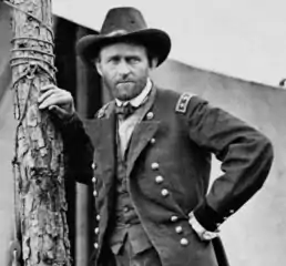 Photograph of Grant in uniform leaning on a post in front of a tent