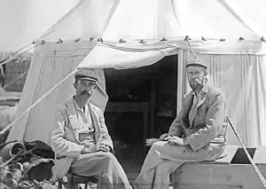 Two men sat in front of an open tent.