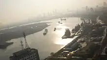 A curving river at dusk lit with diffuse light. Ships and docks can be seen on the river