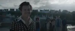 Harry Styles smiling with five other people in the background.