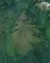 A large lightly glaciated mountain mass surrounded by vegetation and two rivers.