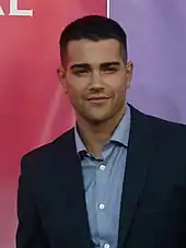 Crew cut: top, short; back/sides, short taper; sideburns, semi-short; short pomp (pompadour) front, arched; mid top, rounded; crown, rounded; front hairline, slightly asymmetric with a cow lick at off center right; wavy hair.