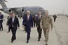Photo of Biden and staffers walking on a tarmac, with a military plane in the background