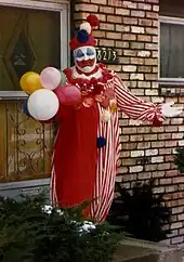 heavy set man in clown costume, with balloons and waving