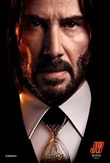 A closeup of John Wick, wearing a hourglass as a "tie", with bullets flowing into the lower bulb inside the hourglass.