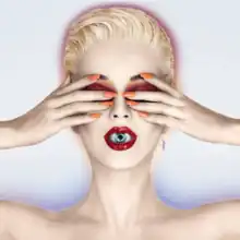 Katy Perry with blonde short hair. She covers her eyes with her hands; an eyeball is visible inside her mouth as her lips are slightly parted.