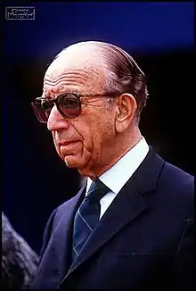 a balding man in a suit and tie, wearing sunglasses, slightly turned to the right