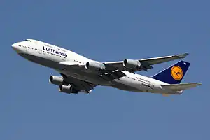 A large white and blue four-engine jet airliner with union tail fin, with landing gear extended