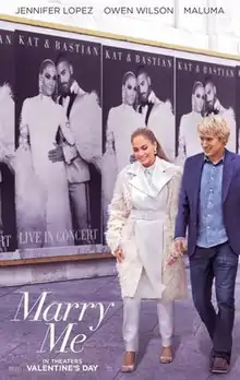 A man and a woman walks past a concert poster featuring the woman.