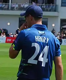 A head and shoulders photograph taken from behind of a cricketer fielding whilst  wearing a blue uniform with the number 24 on his back