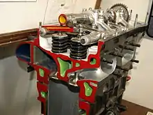 A sectioned, parallel valve, aircraft engine cylinder head is shown with colour-coded internal details. Coolant passageways are painted green; the valves, valve springs, camshaft and rocker arms are also shown.