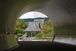 A curving circular tunnel opens to reveal a building with a tall sloping roof and a circular window in the front door.