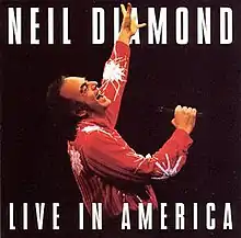 above the waist shot of a man in a red shirt singing with his left arm raised high (the man in red is Neil Diamond)