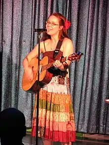 A woman with a guitar standing in front of a microphone
