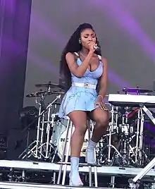 Normani holds a microphone in her hand, looking right and smiling
