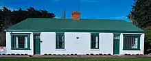 A pair of joined white brick cottages with a common green iron roof