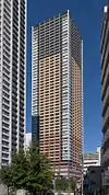 Ground-level view of a rectangular, window-dotted high-rise; the facades are tri-colored with white, beige and gray areas