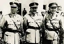Georgios Papadopoulos stands in military uniform, flanked by two other men in uniform