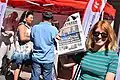 A woman with a Proletären newspaper with a stand used by the Communist Party during the Hammarkullekarnevalen&nbsp;[sv] in 2018.