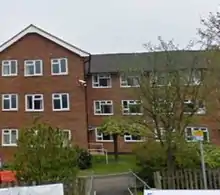 A large, three storey brick building with some trees and bushes in the foreground.