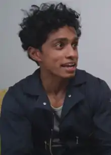 Rajiv Surendra wearing dark, zippered jacket, appearing to speak and looking left of camera