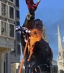 A statue of Frank Rizzo covered in red spray paint with a burning American flag attached to it